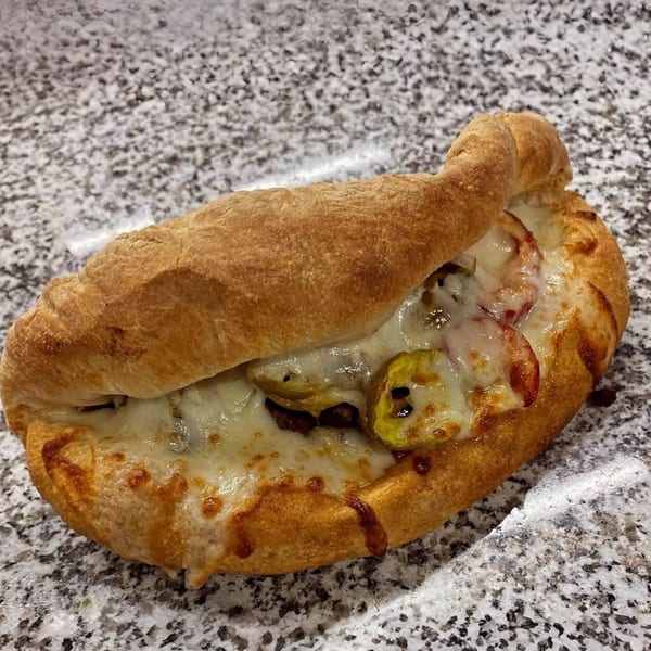 A golden-brown calzone from Clarksburg Pizza Co. filled with melted cheese, meat, and peppers.