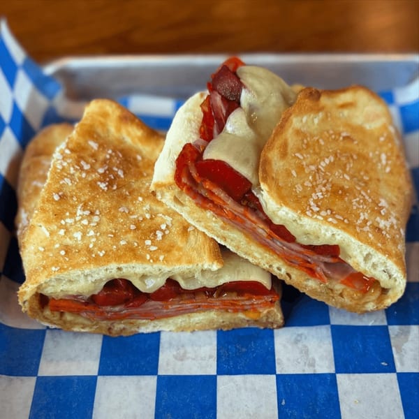 Three Italian sandwiches with melted cheese, pepperoni, and red peppers in a blue and white checkered basket.