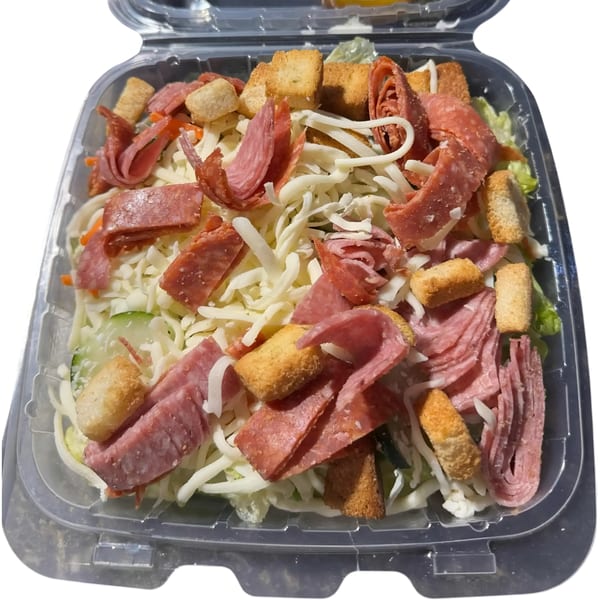 Italian salad with salami, pepperoni, shredded cheese, and croutons in a clear plastic container.