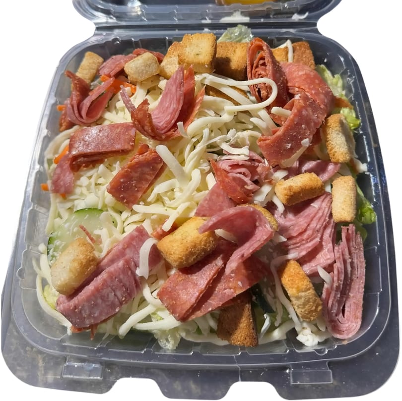Italian salad with salami, pepperoni, shredded cheese, and croutons in a clear plastic container.