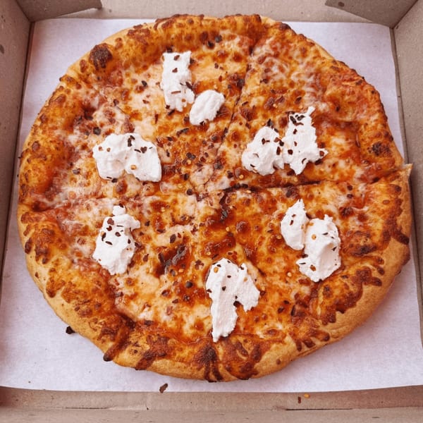 A whole pizza from Clarksburg Pizza Co. with melted cheese, red pepper flakes, and dollops of ricotta cheese.