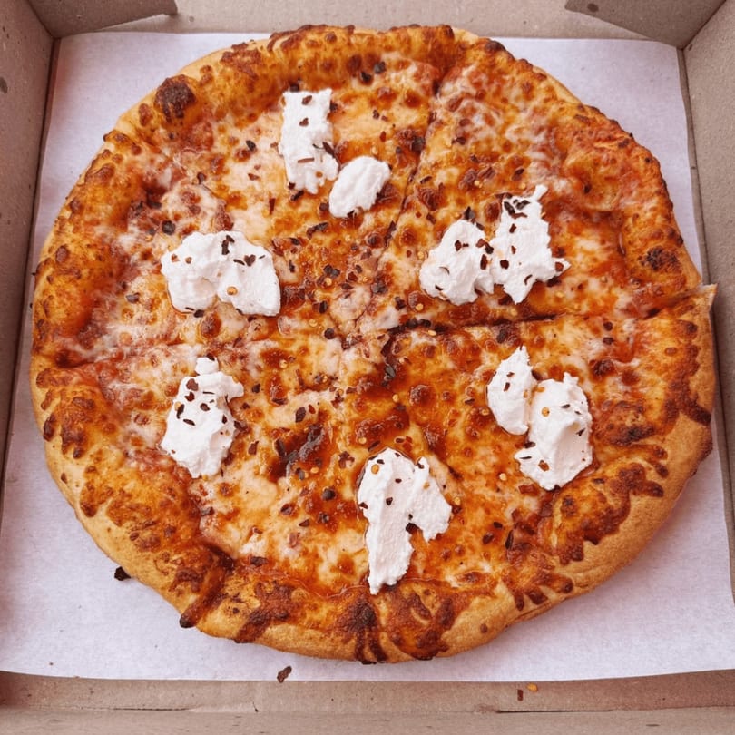 A whole pizza from Clarksburg Pizza Co. with melted cheese, red pepper flakes, and dollops of ricotta cheese.