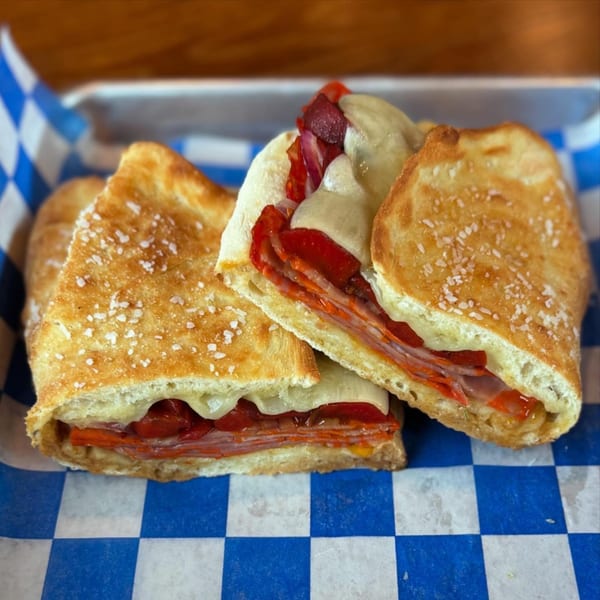 Three Italian sandwiches with meat, cheese, and peppers, served in a blue and white checkered basket.
