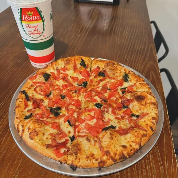 A Clarksburg Pizza Co. pizza with diced tomatoes and basil, next to a Roma branded cup.